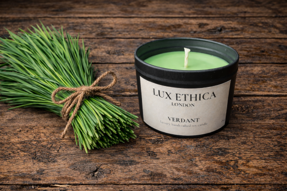 Green scented candle beside fresh chives on a wooden table.